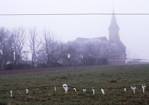 Silhouette silencieuse de l'église de Mecleuves émergeant du givre et de la brume