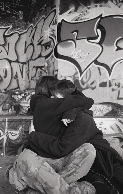 L'accolade du Bowl Photographie intime en noir et blanc de deux jeunes s'entrelaçant chaleureusement, assis sur le béton du skatepark.