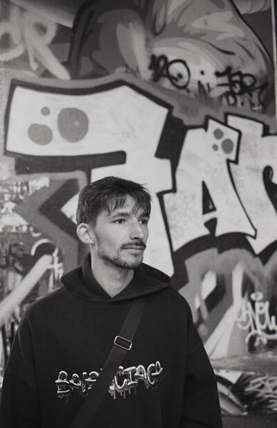 Le guetteur du Bowl Portrait de profil d'un jeune homme à moustaches portant un sweat à capuche Balenciaga, regardant pensivement au loin devant des graffitis.