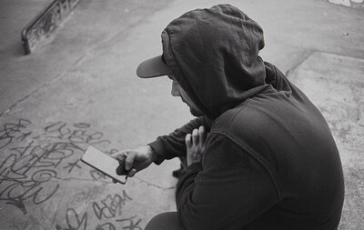 Instant connecté Vue en plongée d'un skateur solitaire en sweat à capuche, accroupi sur le béton et consultant son smartphone.